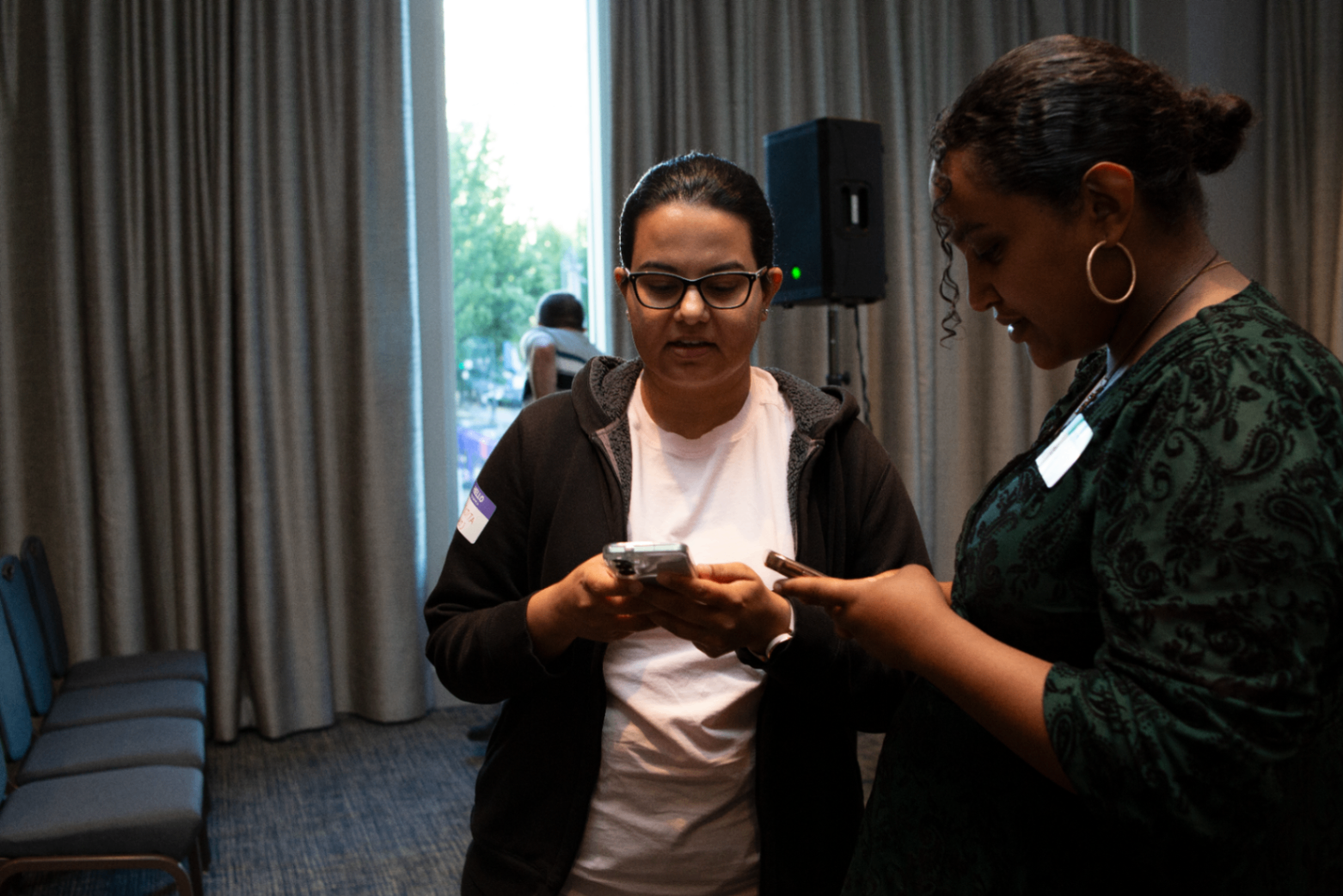 Two attendees checking their phones by the event curtains